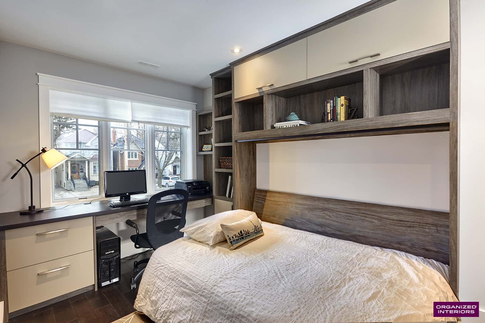 Double side tilt Murphy bed in Sand Beige and Sunset Cruise with ample overhead storage by Organized Interiors. Small bedroom with Murphy bed in down position, computer, desk, and chair, custom built-ins.