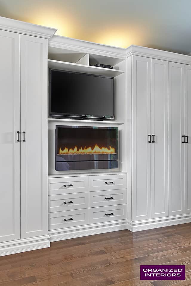 Cropped photo of mounted TV and electric fireplace in white custom builtin cabinetry.